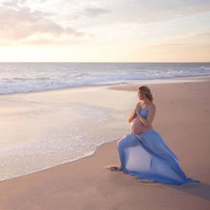 A pregnant woman in a blue dress on the beach.