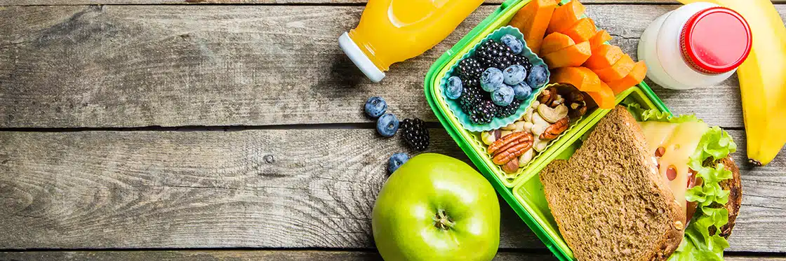 A lunch box with fruits and vegetables on a wooden table.